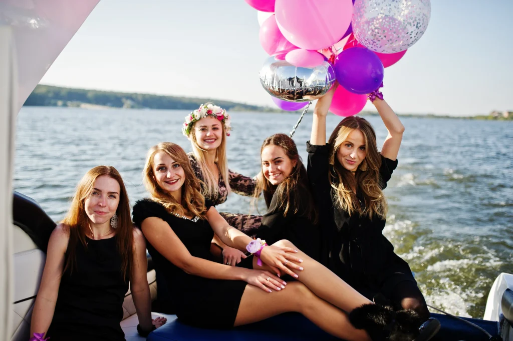 Group of women celebrating on boat with colorful balloons, enjoying party on water outdoors