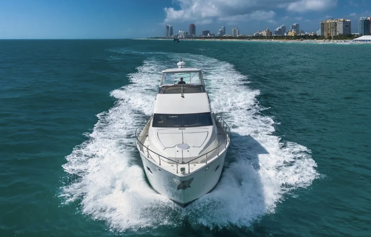 Luxury yacht cruising toward city skyline on clear blue ocean with foamy